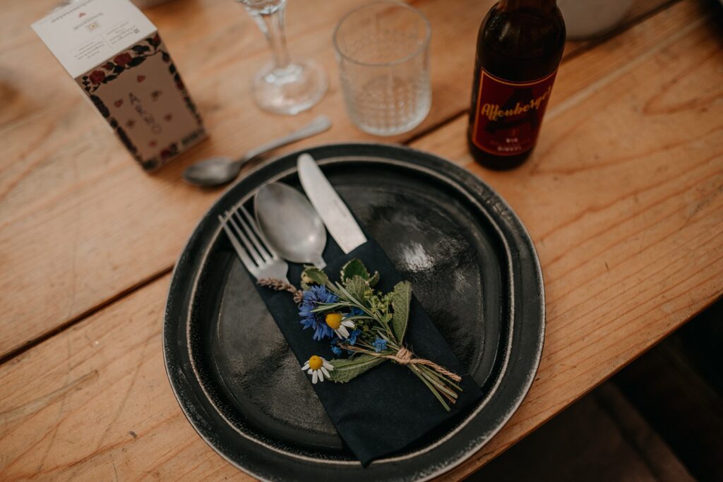 Gedeck mit dunklem Teller und Wiesenblumen auf der Holztafel