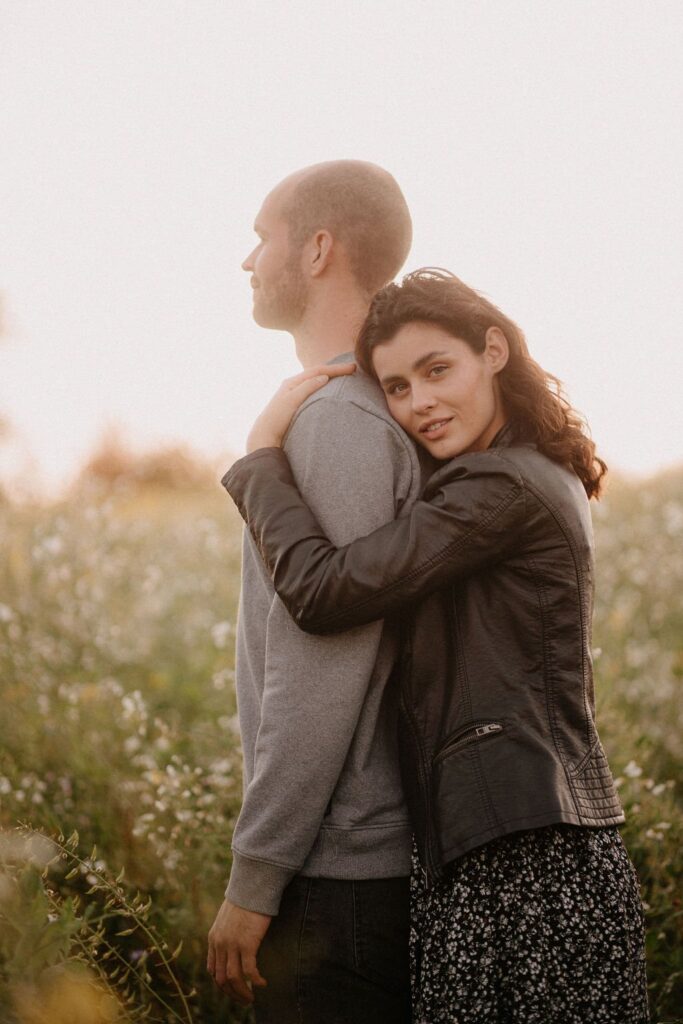 Bianca umarmt Philipp von hinten in der Blumenwiese