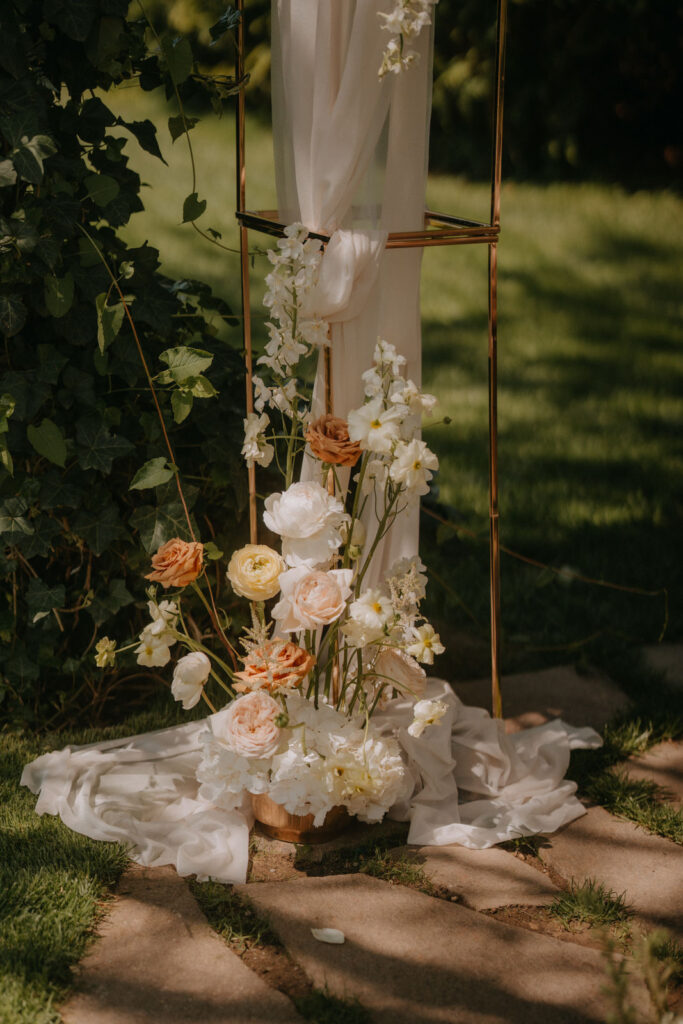 Detailaufnahme eines floralen Gestecks mit weißen Ranunkeln, Pfingstrosen und rostfarbenen Rosen für eine freie Trauung
