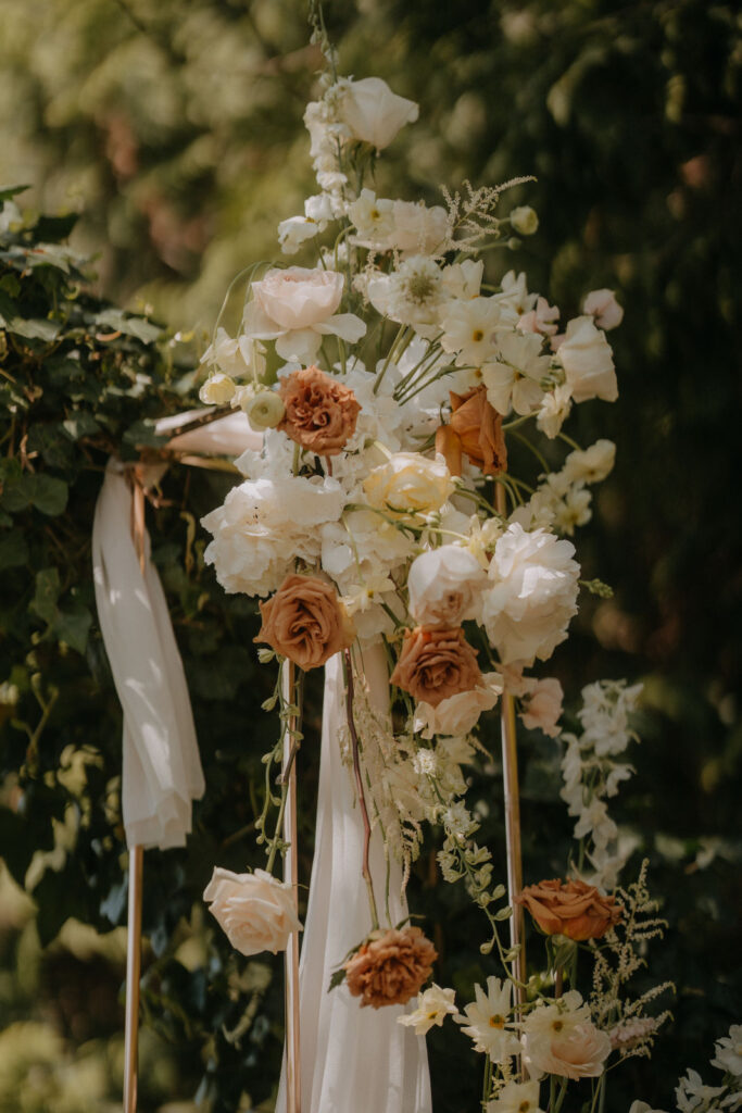 Romantisch gesteckter Blumenbogen mit cremefarbenen und rostigen Tönen für eine elegante Outdoor-Trauung im Frühling