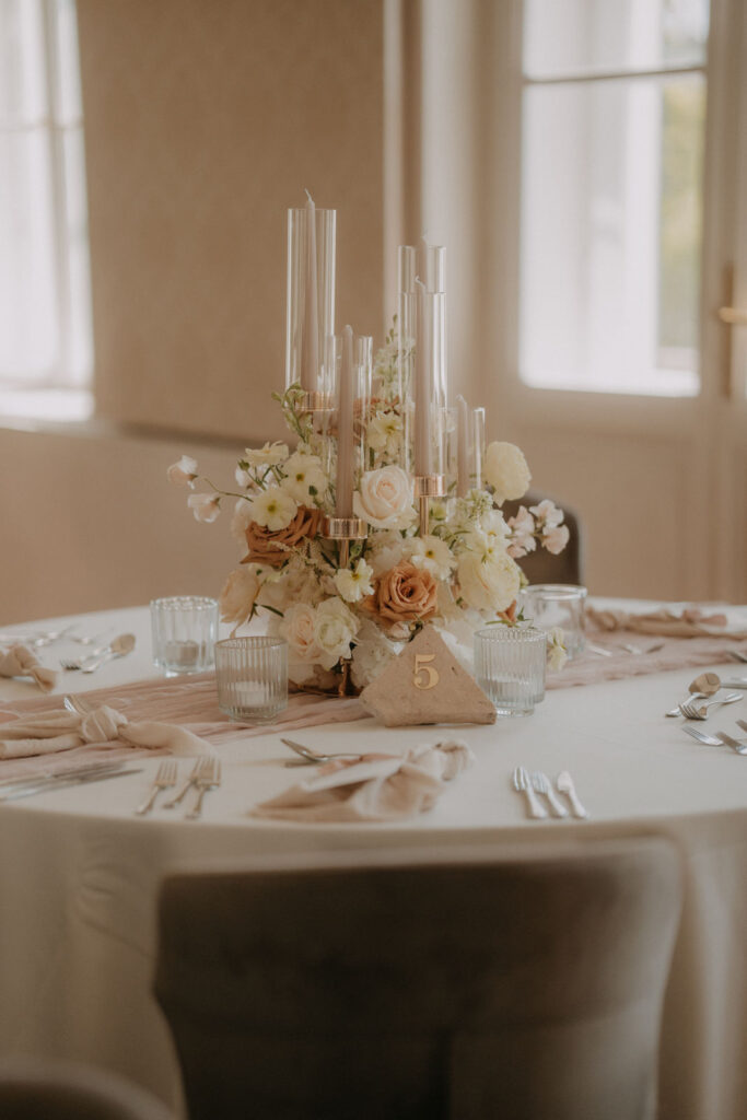 Elegante Hochzeits-Tischdekoration mit floralen Centerpieces in warmen Cremetönen und langen Kerzen im Schloss St. Veit