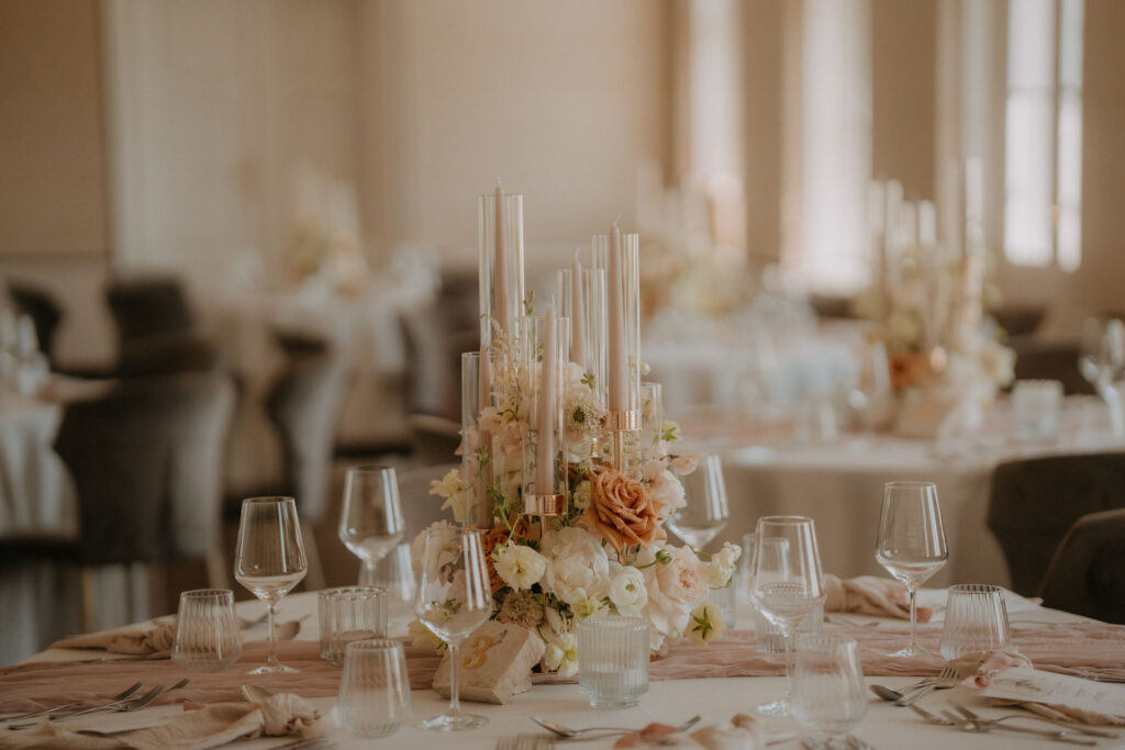 blumengesteck mit langen Stabkerzen auf Hochzeitstisch – zarte Farben in Pfirsich und Creme