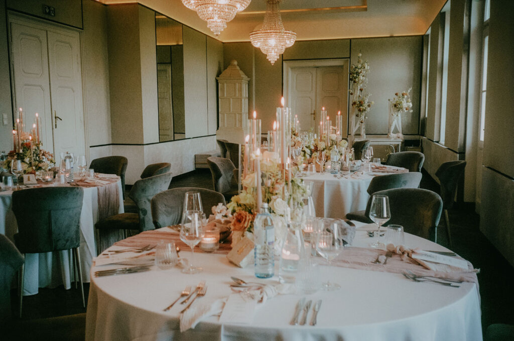 Stilvoll gedeckter Hochzeitstisch mit floraler Mitte und Kerzenschein im Festsaal des Aiola im Schloss St. Veit – aufgenommen auf Portra 400.