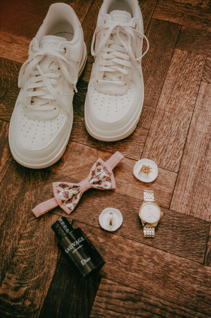 Detailaufnahme der Accessoires des Bräutigams – Fliege, Uhr, Eheringe und Sneakers – liebevoll arrangiert auf Portra 400.