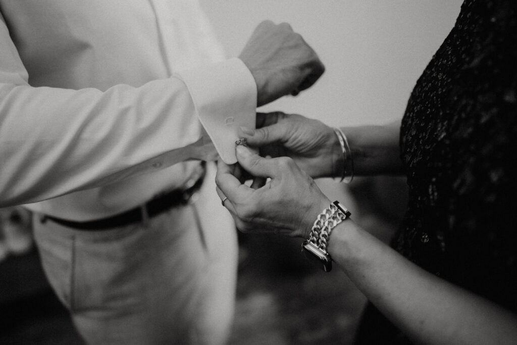 Schwarzweiß-Foto beim Anlegen der Manschettenknöpfe – Getting Ready des Bräutigams am Hochzeitstag im Aiola im Schloss St. Veit.