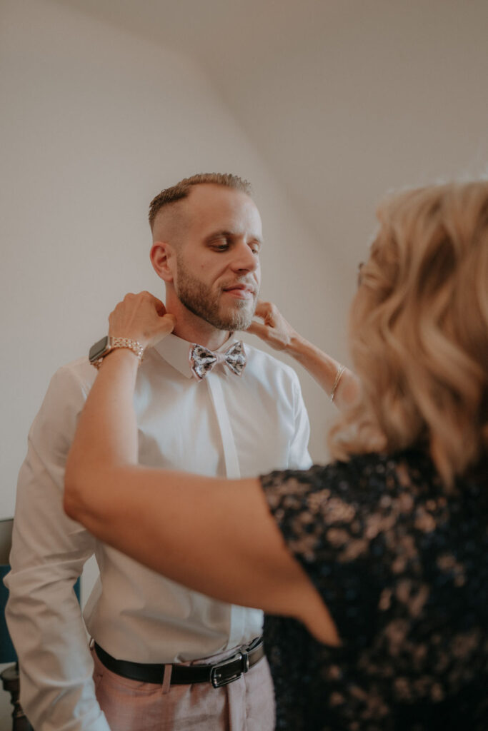Persönlicher Moment: Die Mutter hilft dem Bräutigam beim Anlegen seiner Fliege – Hochzeit von Lizz & Chris im Mai 2025.