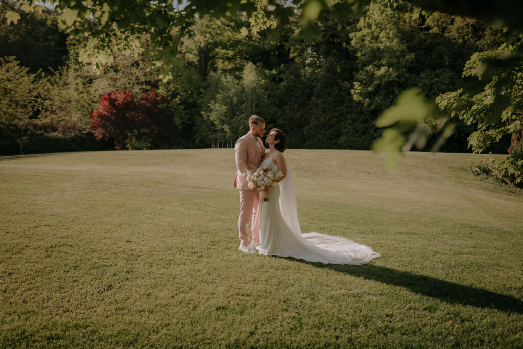 Das Brautpaar Lizz und Chris bei ihrer Hochzeit im Aiola Schloss St. Veit, umrahmt von grüner Parkkulisse.