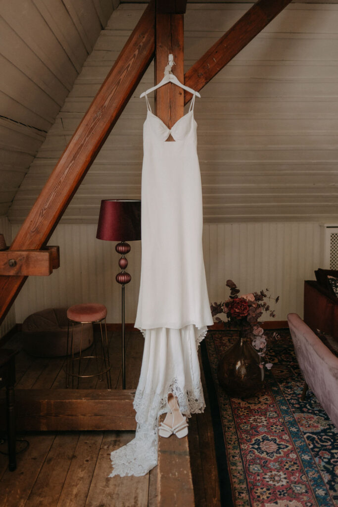 Das Brautkleid hängt an einem Holzbalken in einem stilvollen Ankleidezimmer.