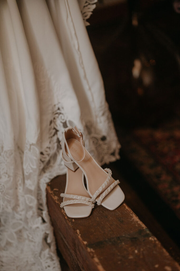 Detailaufnahme der Brautschuhe mit Perlenbesatz, vor dem Spitzenabschluss des Kleides.
