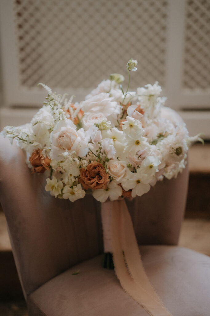 Sommerlicher Brautstrauß mit weißen und rostfarbenen Blüten, elegant gebunden auf einem roséfarbenen Samtsessel