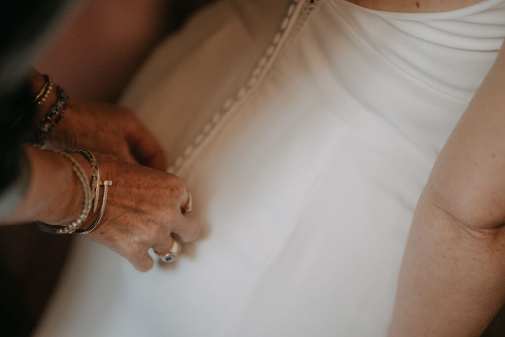 Detailaufnahme einer Hand, die die Knöpfe des Brautkleides schließt.