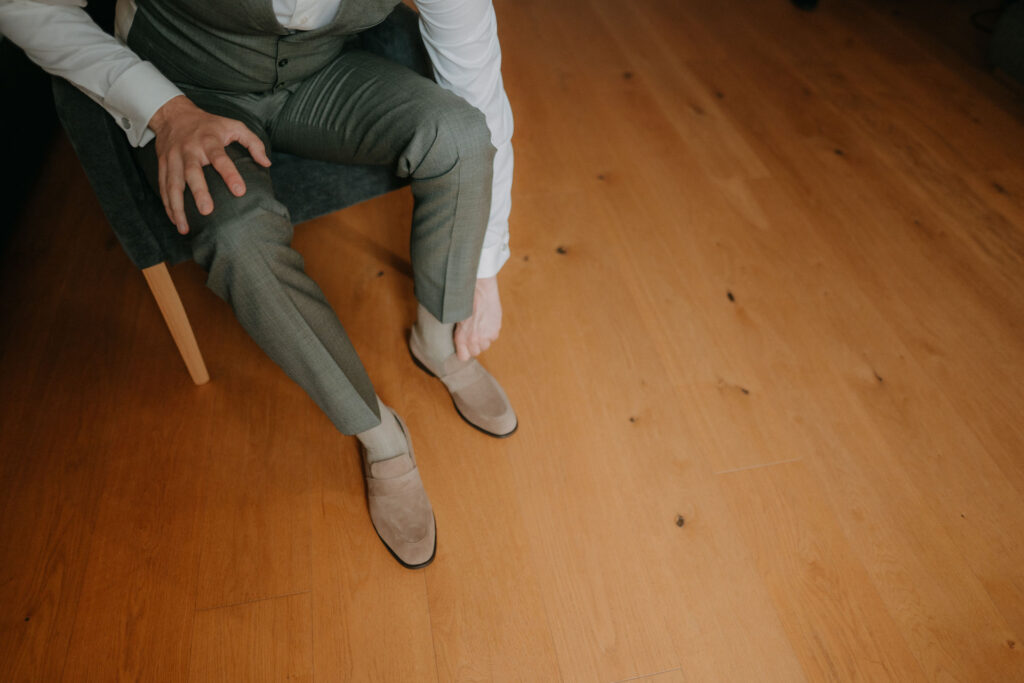 Der Bräutigam sitzt entspannt und zieht seine Schuhe an.