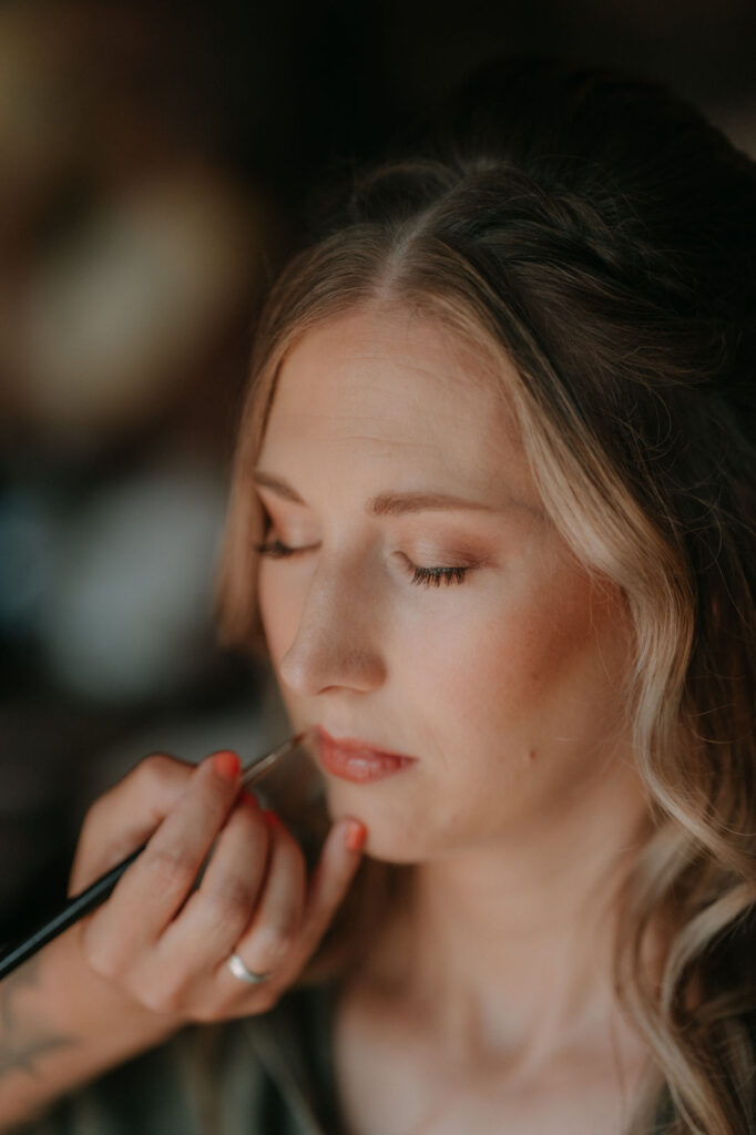 Die Braut wird liebevoll geschminkt, Lippenstift wird aufgetragen.