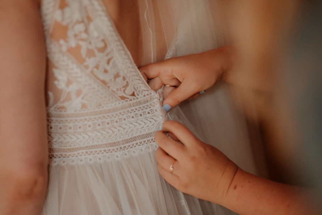 Detailaufnahme vom Schließen der Knöpfe am Brautkleid.