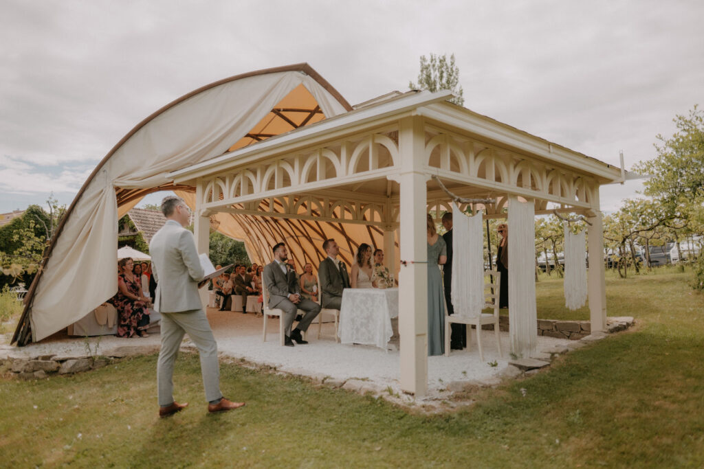 Blick auf den weißen Pavillon, der festlich geschmückt und von Freunden und Familie umgeben ist.