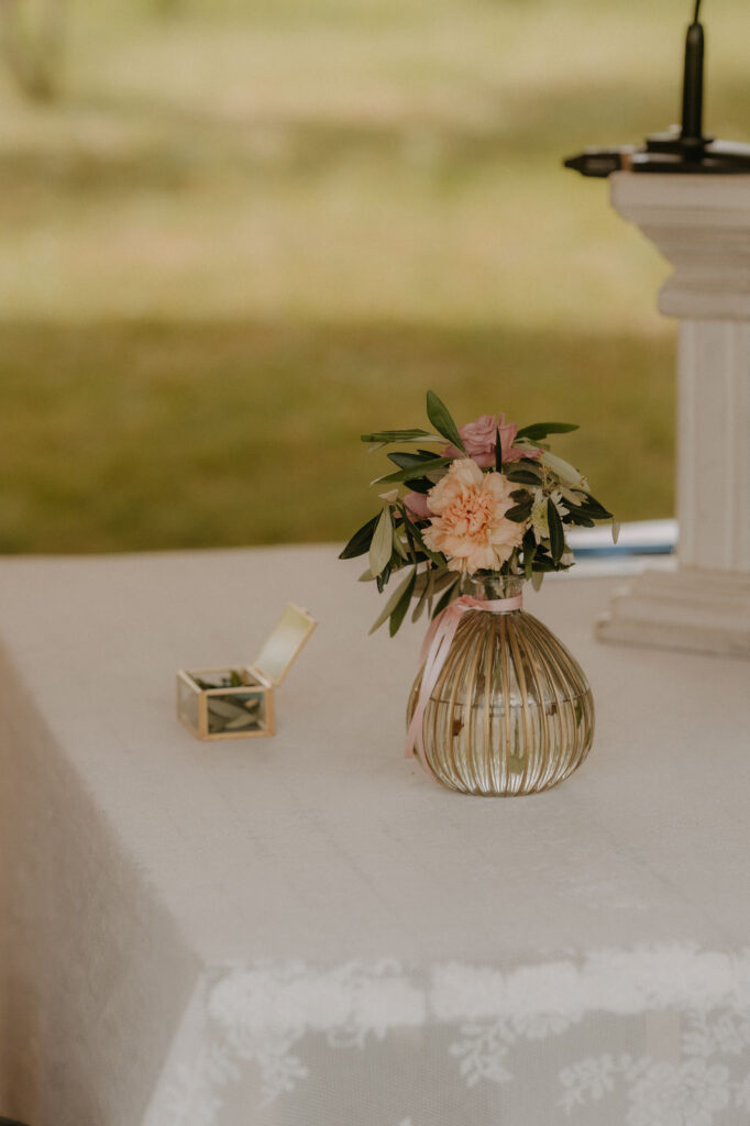 Detailfoto des Brautstraußes in einer eleganten Vase, der Trauungstisch schlicht dekoriert.
