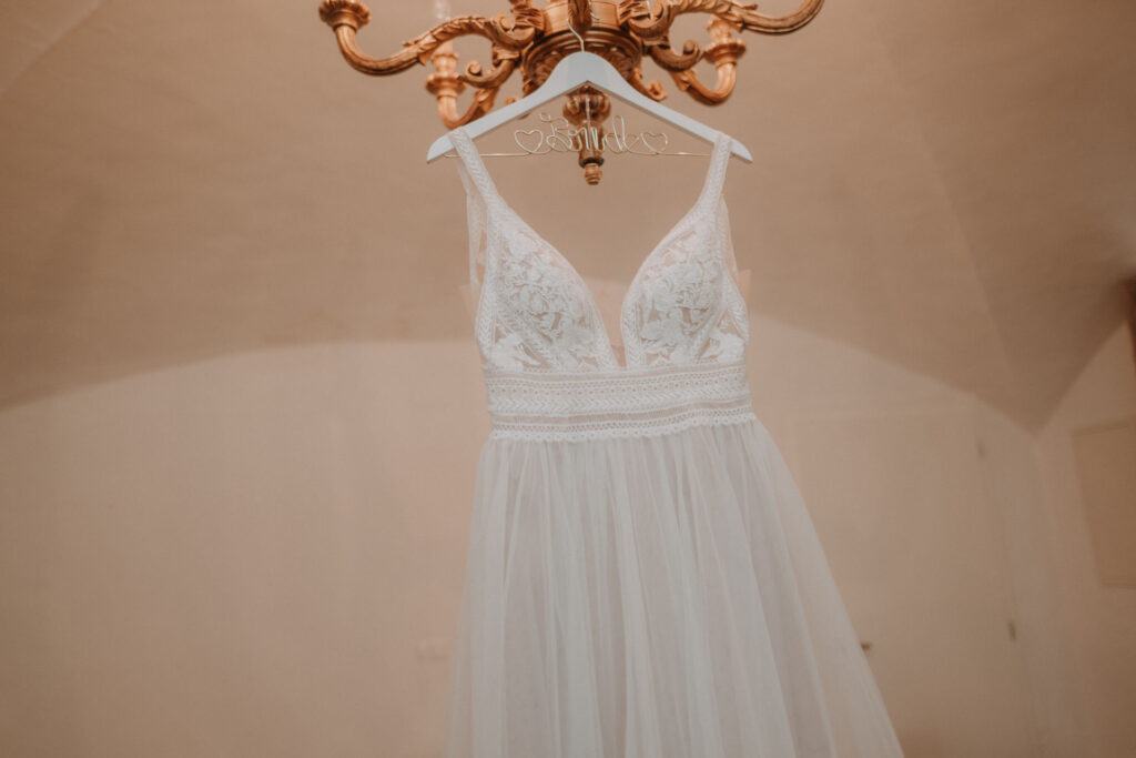Ein elegantes Brautkleid hängt an einem goldenen Kleiderbügel, umgeben von floralen Details.
