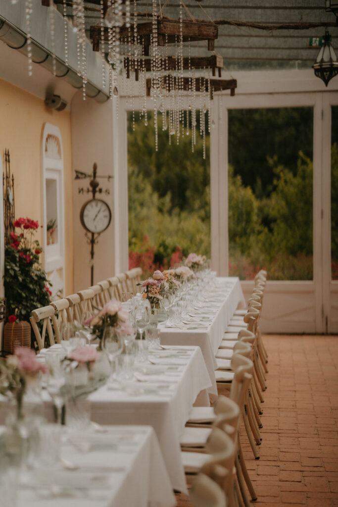 Langer, elegant gedeckter Tisch unter einer Pergola, umgeben von grünem Garten und warmer Atmosphäre.
