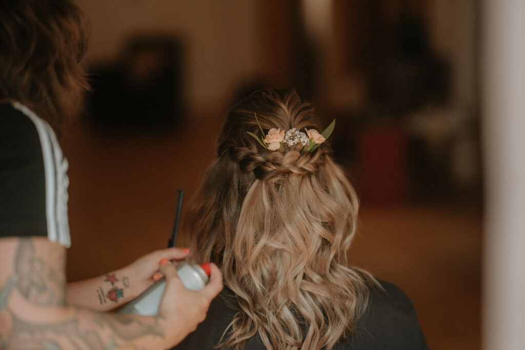 Die Braut bekommt ihren Haarlook vollendet – mit kleinen Blumen im Haar.