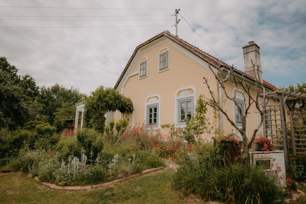 Romantisches Landhaus mit gelber Fassade, umgeben von Blumen und Natur, perfekte Kulisse für eine Hochzeit.