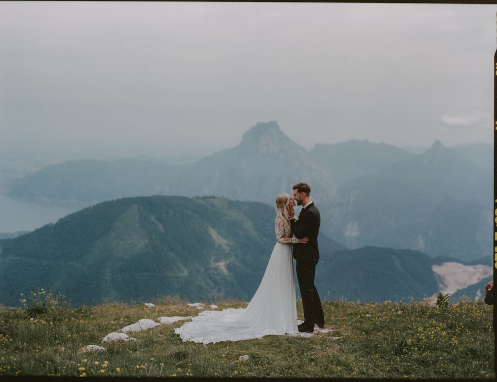 Das Brautpaar steht eng umschlungen auf einem Wiesenplateau mit Blick auf den Traunstein und das Alpenpanorama.