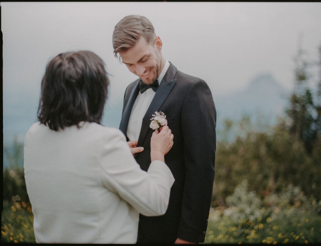 Die Mutter des Bräutigams steckt ihm die Ansteckblume an, im Hintergrund die Berge.