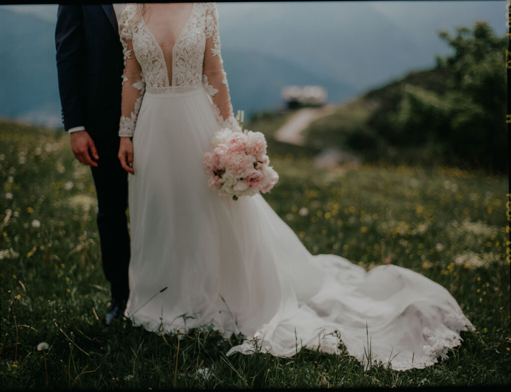 Nahaufnahme von Brautkleid, Brautstrauß und Details des Paars vor alpiner Kulisse.