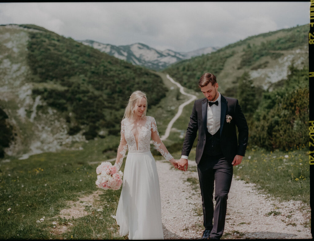 Julia & Wolfgang gehen Hand in Hand über einen schmalen Bergpfad im Salzkammergut nach ihrer freien Trauung