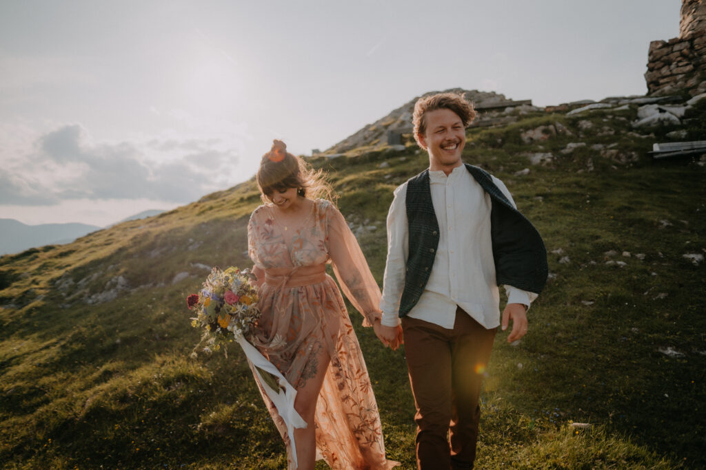 aar läuft lachend Hand in Hand über eine Bergwiese bei goldenem Abendlicht – authentische Hochzeitsfotografie in der Steiermark von Pixellicious Fotografie