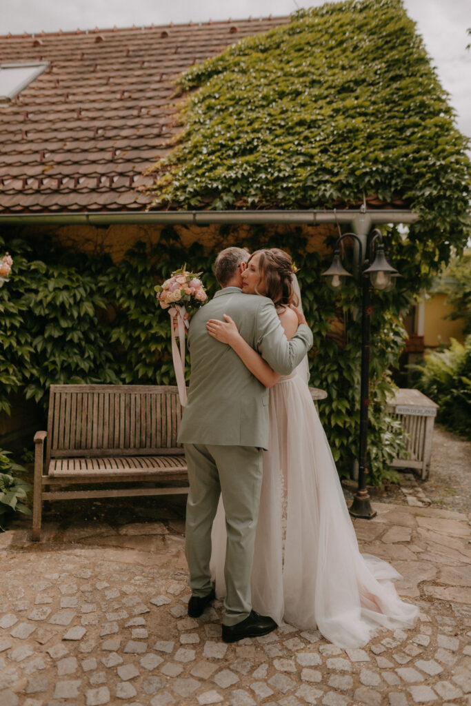 Emotionaler First-Look-Moment zwischen Braut und Papa im Hof einer romantisch bewachsenen Hochzeitslocation in der Steiermark