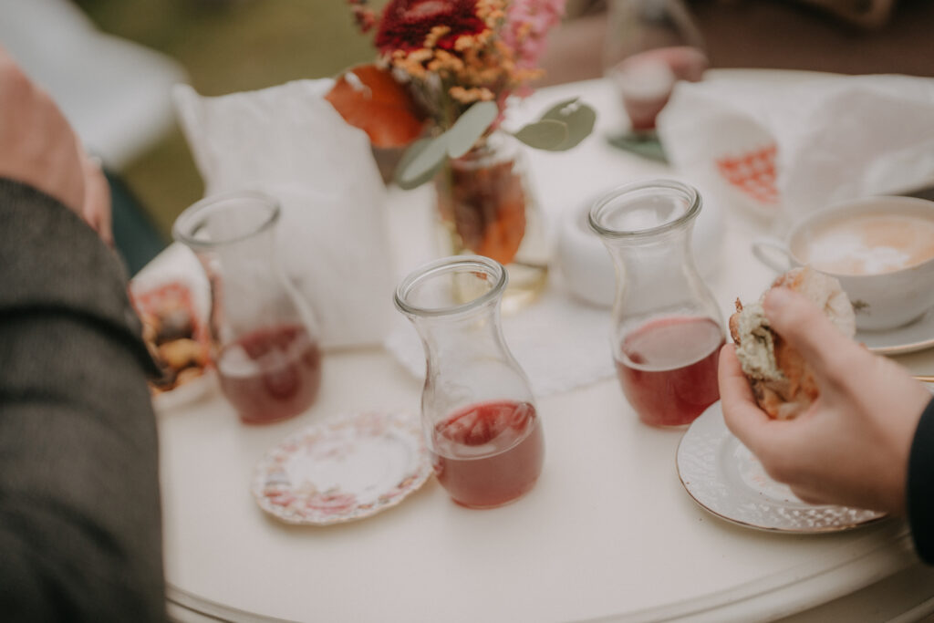 Herbstliche Agape bei einer Waldhochzeit in der Steiermark mit kleinen Glaskaraffen voller rotem Saft und Gästen, die Snacks genießen.