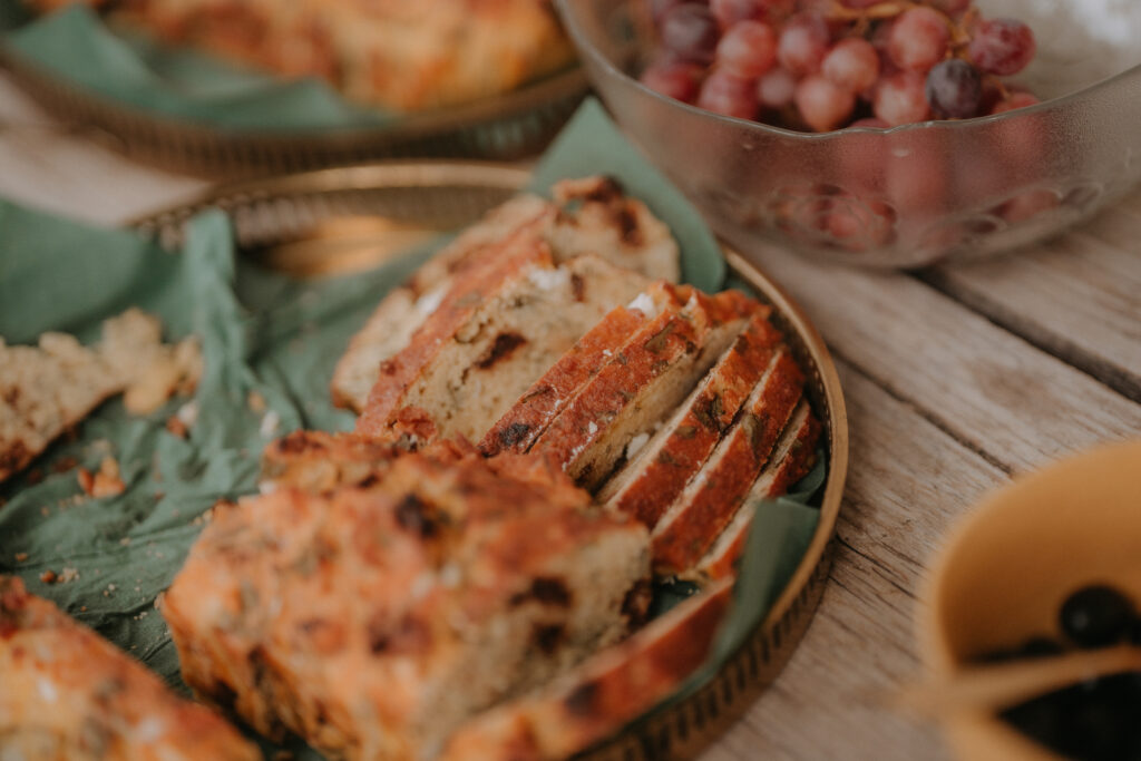 Herzhaftes Hochzeitsbuffet mit frisch geschnittenem pikantem Kuchen und einer Schale roter Trauben bei einer Waldhochzeit in der Steiermark.
