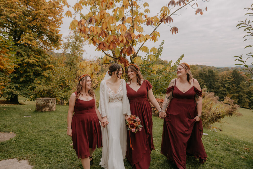 Braut und Brautjungfern spazieren lachend durch den herbstlichen Garten.