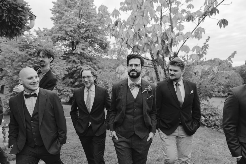 Bräutigam geht lachend mit seinen Freunden durch den Garten, festgehalten in einer schwarz-weiß Aufnahme.