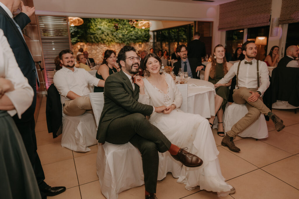 Braut und Bräutigam sitzen eng aneinander während der Hochzeitsfeier und lachen gemeinsam – emotionale Momentaufnahme bei der Waldhochzeit in der Steiermark.