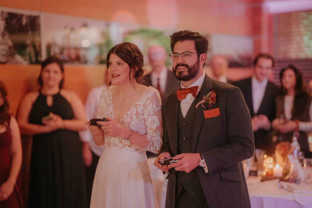 Braut und Bräutigam spielen lachend ein Partyspiel mit Controller – moderner, persönlicher Moment während der Hochzeitsfeier in der Steiermark.