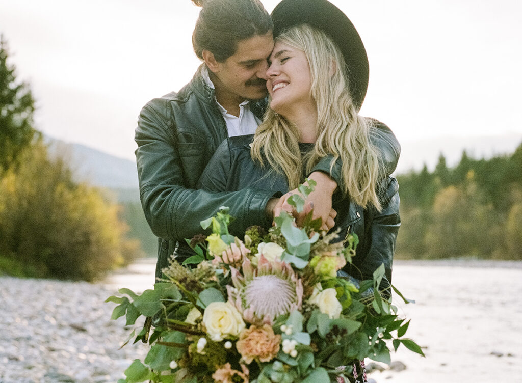 Paarshooting in der Natur mit Blumenstrauß und Bergen im Hintergrund