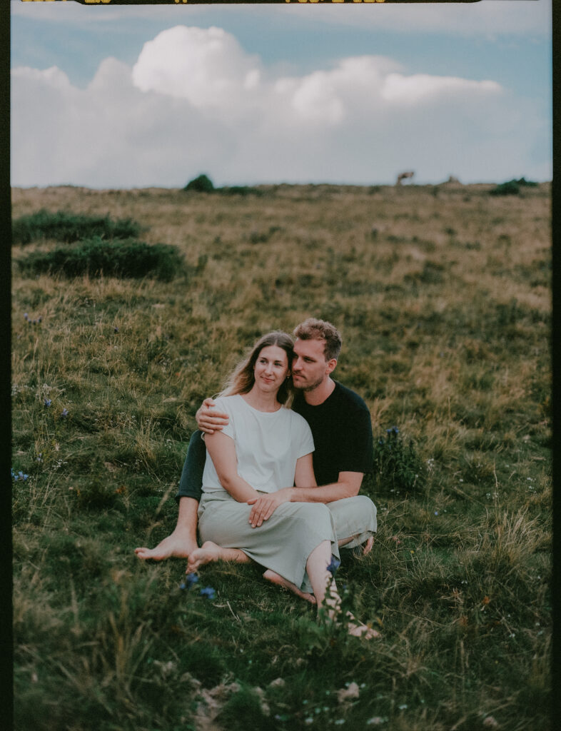 Paar sitzt in Bergwiese – analoge Paarfotografie in der Natur
