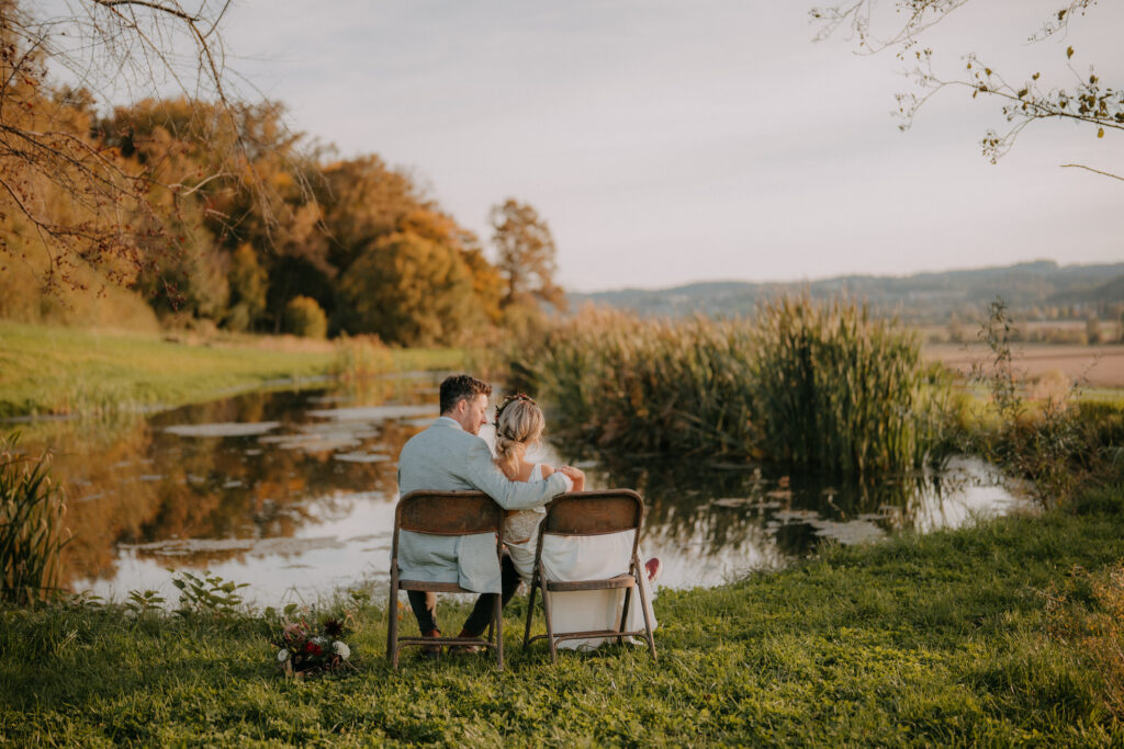 Brautpaar sitzt auf zwei Stühlen mit Blick auf See