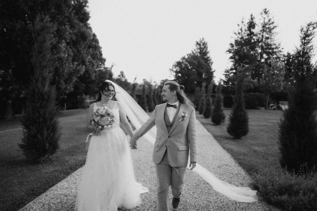 Brautpaar spaziert Hand in Hand durch die Allee im Schlosspark Ottersbach – schwarz-weiß Hochzeitsfoto Steiermark
