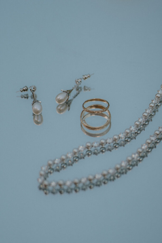 Schmuck der Braut – Perlenkette, Ringe und Ohrringe auf hellblauem Hintergrund