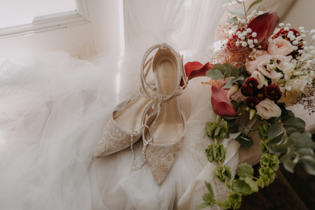 Brautschuhe mit Spitze und Perlendetail neben Brautstrauß