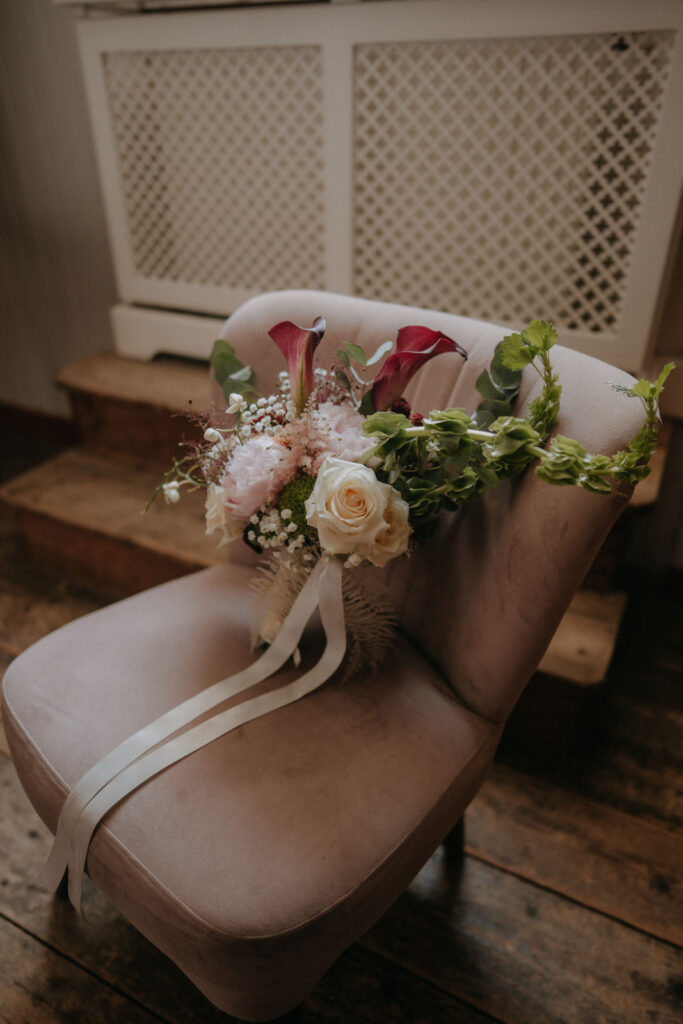 Brautstrauß mit roten Callas und Pfingstrosen auf rosa Samtsessel – Hochzeit Aiola Graz
