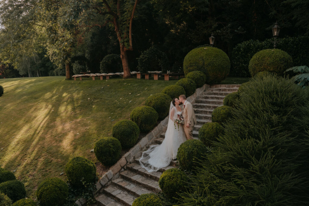 Brautpaar küsst sich auf der Gartentreppe mit Buchskugeln – Hochzeit Aiola im Schloss Graz