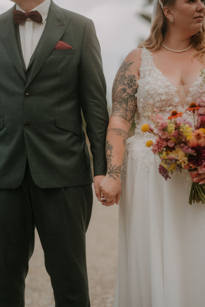 Detailaufnahme von Brautpaar Hand in Hand mit buntem Brautstrauß bei der Hochzeit auf Schloss Ottersbach