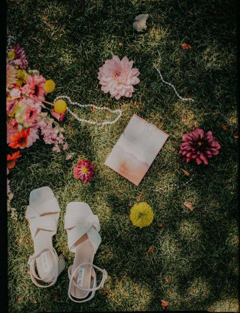 Analoges Flatlay mit weißen Brautschuhen und bunten Blumen im Gras auf Schloss Ottersbach