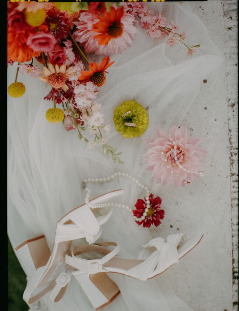 Analoge Nahaufnahme von Brautschuhen mit Perlenkette und Dahlien auf dem Schleier, Schloss Ottersbach