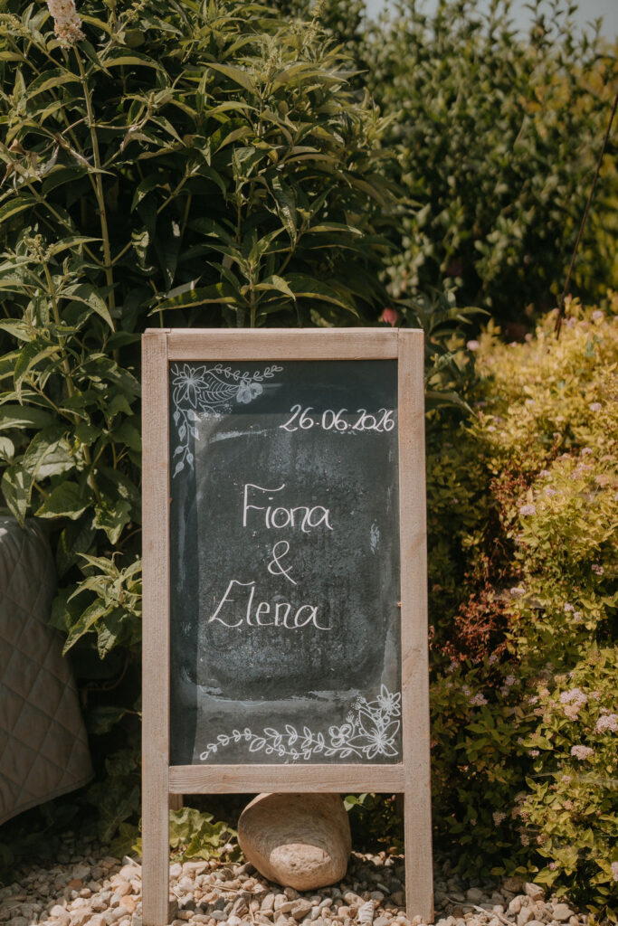 Kreidetafel mit Namen des Brautpaars und Hochzeitsdatum im Garten