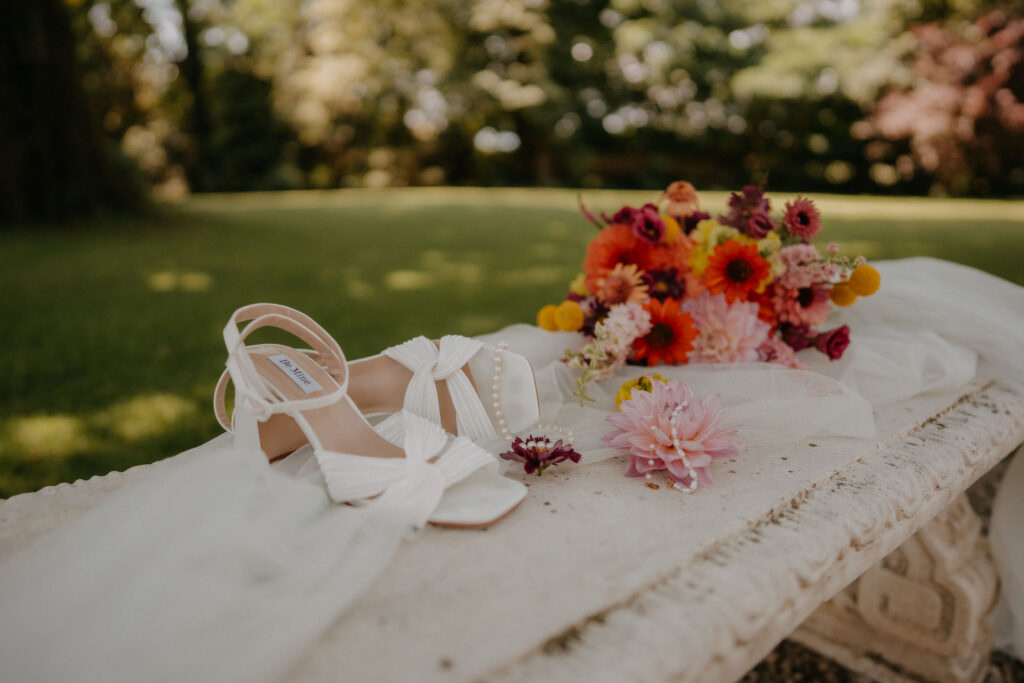 Weiße Brautschuhe neben buntem Blumenstrauß auf der Wiese von Schloss Ottersbach