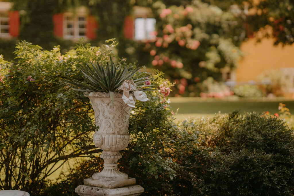 Blick auf den Garten von Schloss Ottersbach mit steinerner Pflanzvase und blühenden Rosenbüschen
